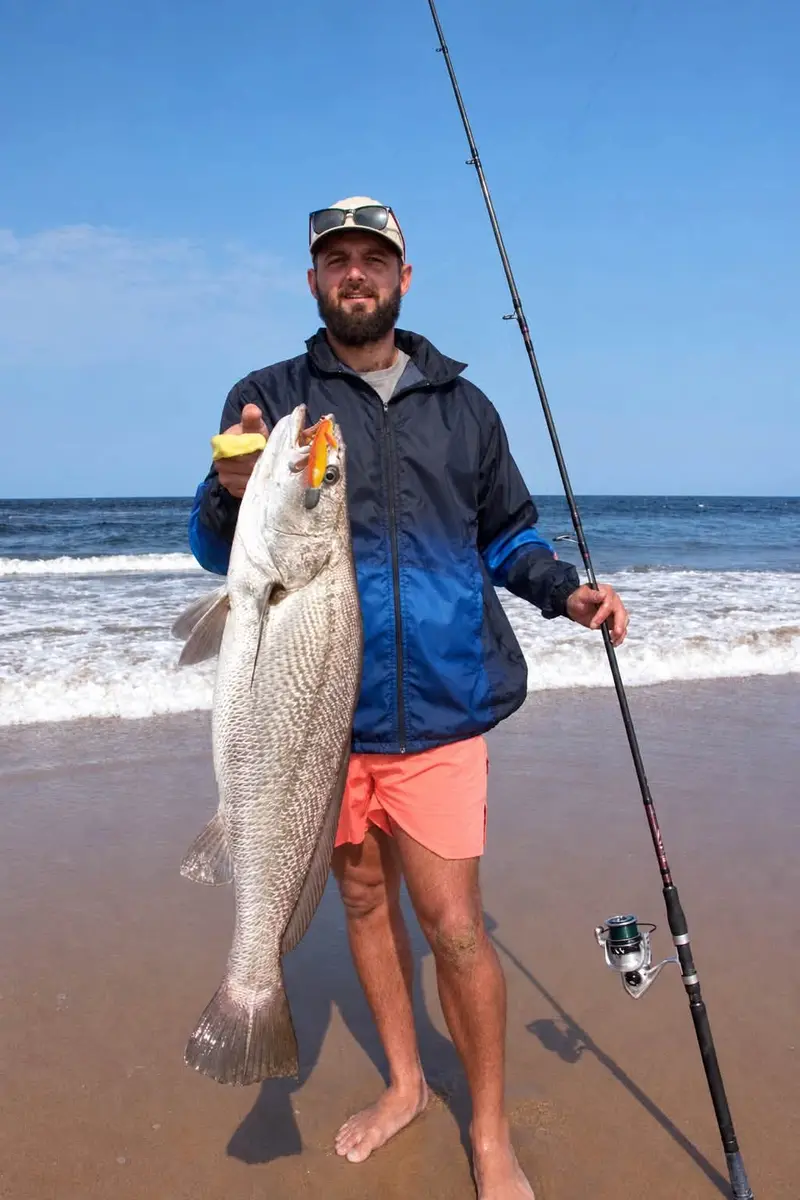 Angler standing on the beach with a kob under a sunny blue sky